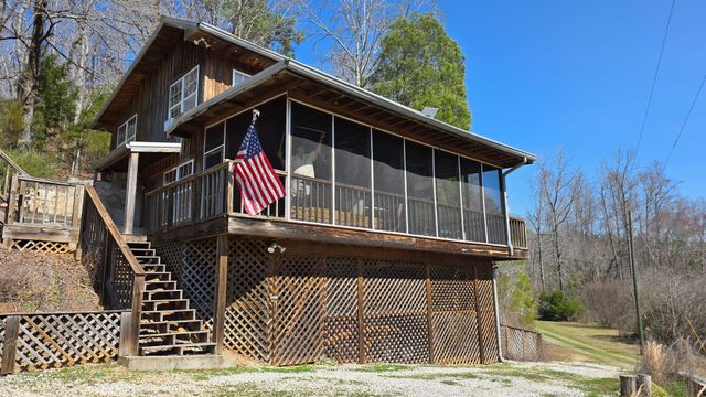 Rustic cabin with screened porch, American flag, and exterior stairs on a wooded hillside