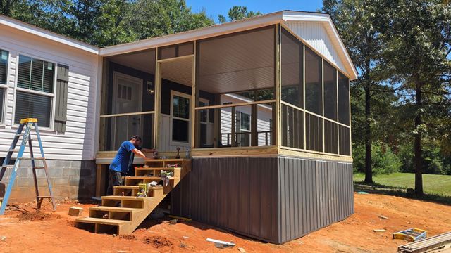 Single-story brick house with workers renovating the front yard, ladders, tools, and scattered materials.