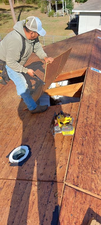 Worker on a roof repairing brown shingles with tools nearby.