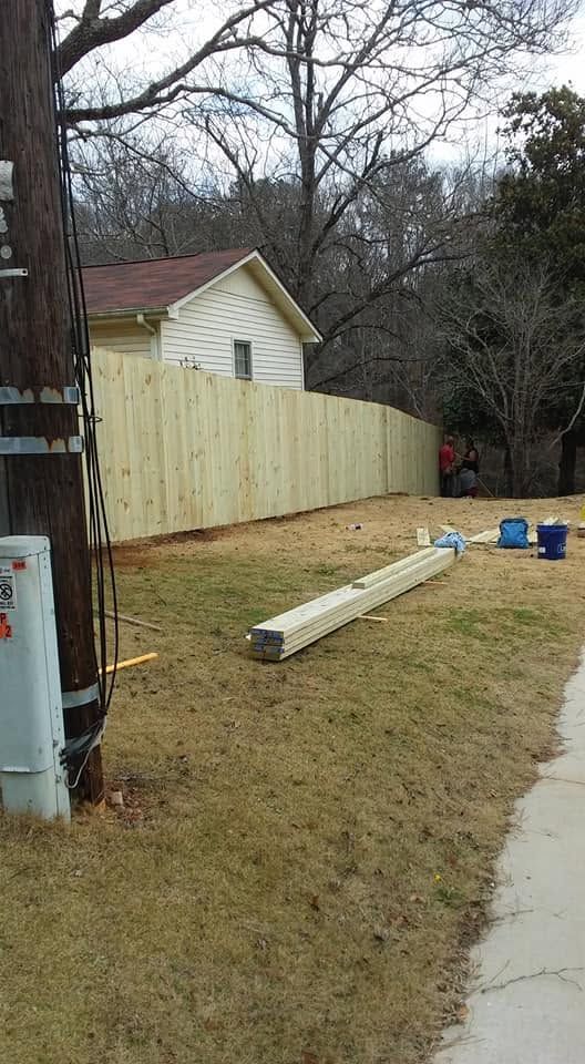 Residential yard with a leaning white fence, fallen white post, sidewalk, and bare trees on a cloudy day