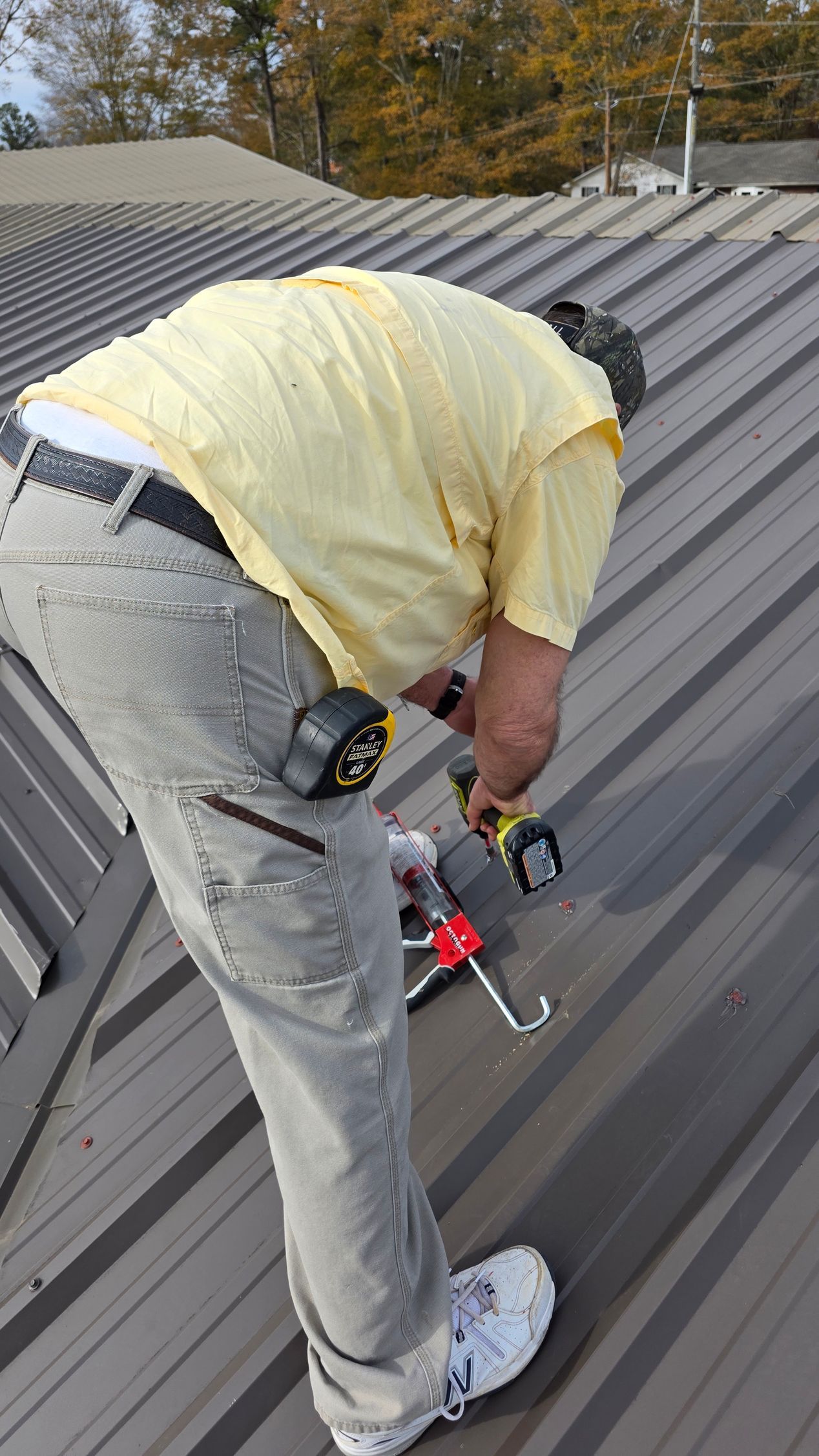 Worker in yellow shirt using a tool on a gray metal roof