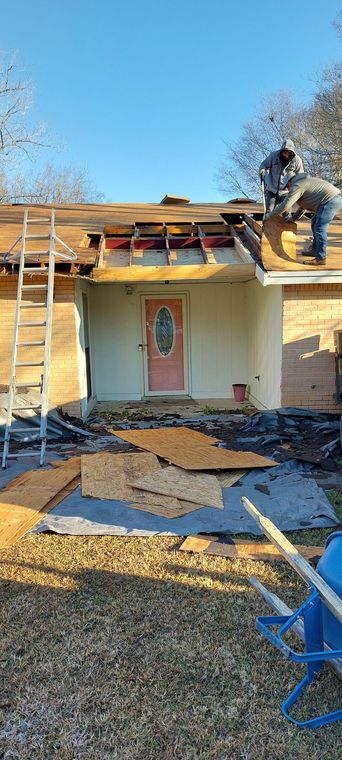 House under roof repair with ladder, worker on top, and construction materials in front yard