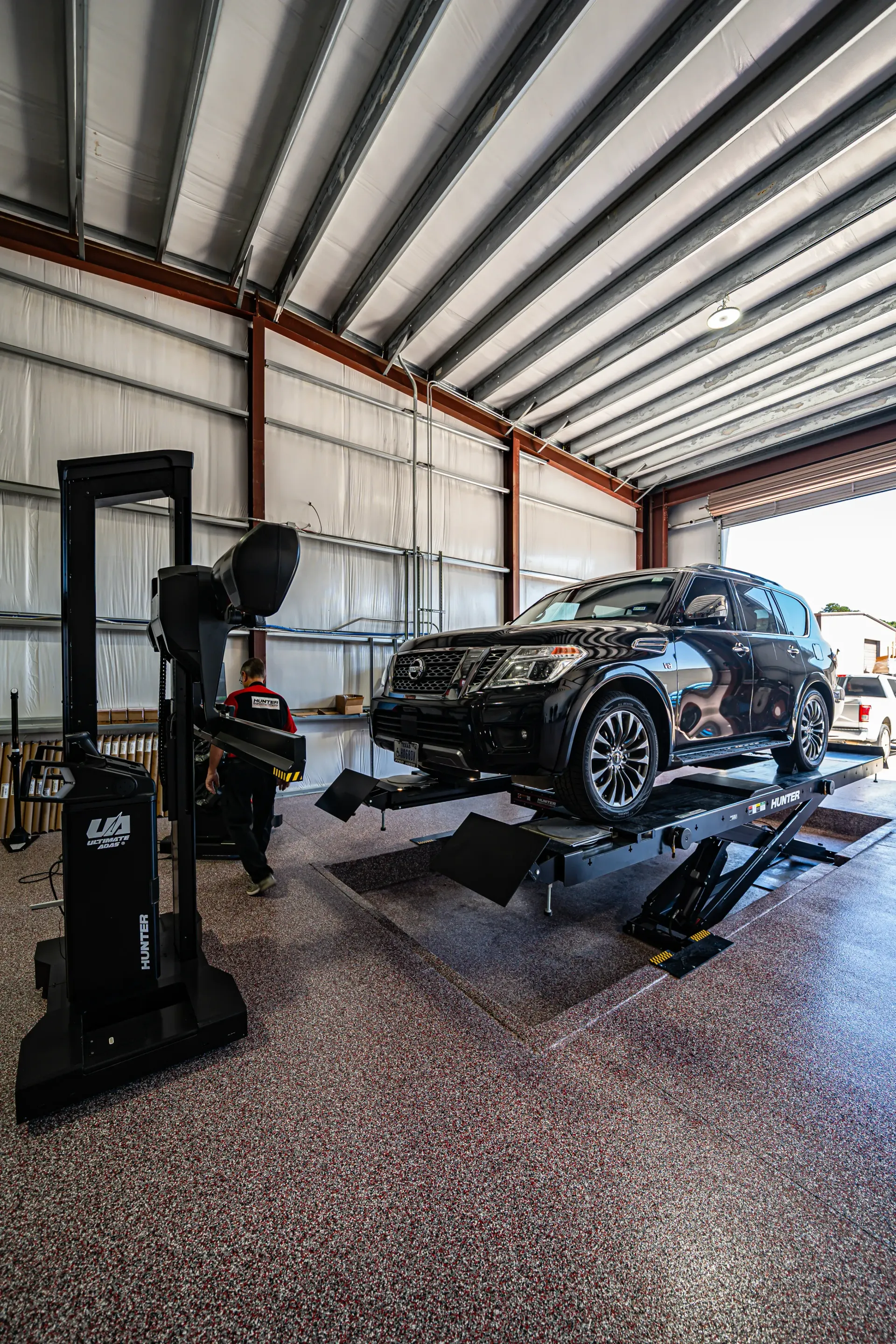 Black SUV on a lift in a garage, undergoing wheel alignment. Alignment equipment is in view. | Advance Automotive