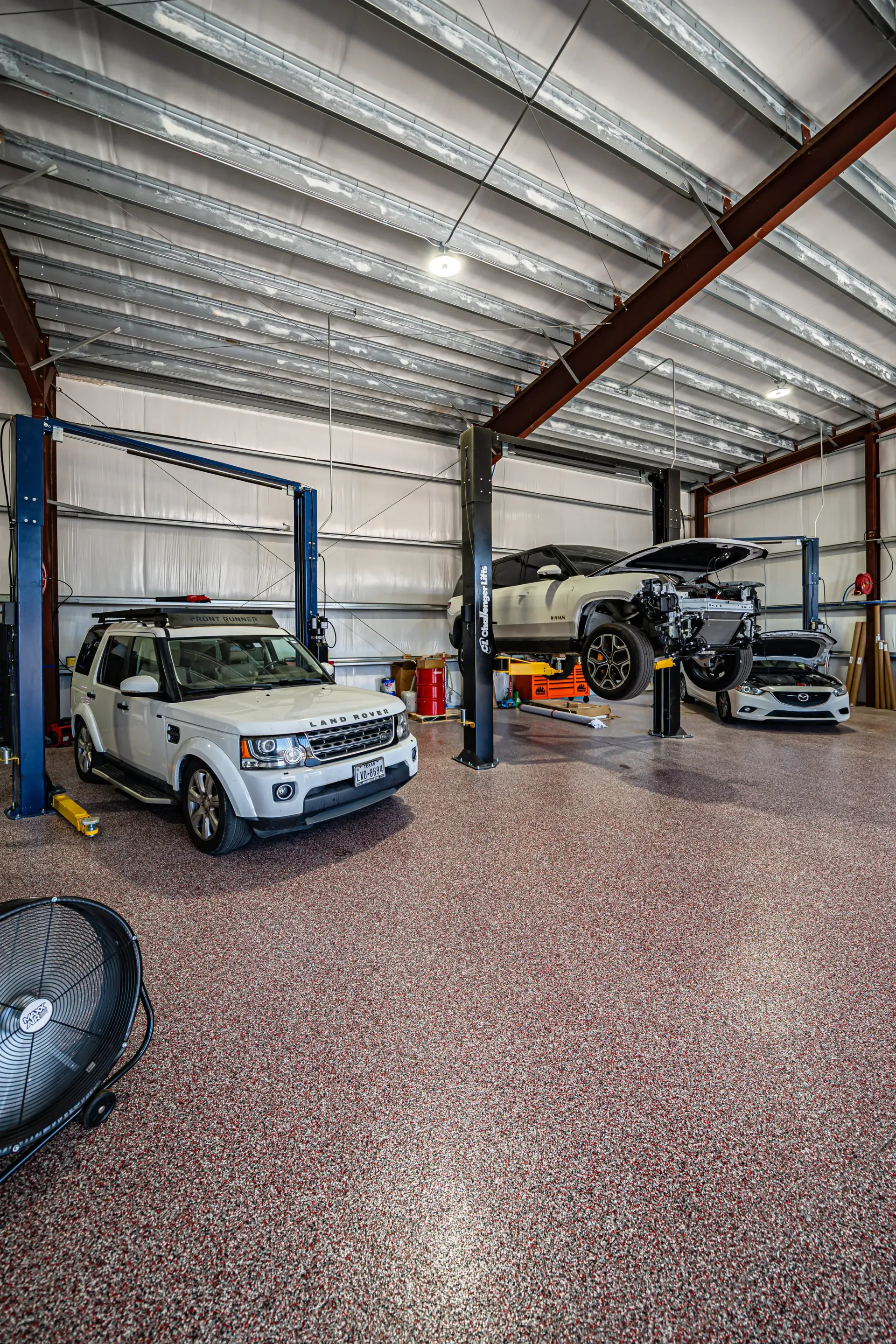 A garage with red-speckled floors. Several SUVs are parked or lifted by a car lift. The ceiling is metal. | Advance Automotive