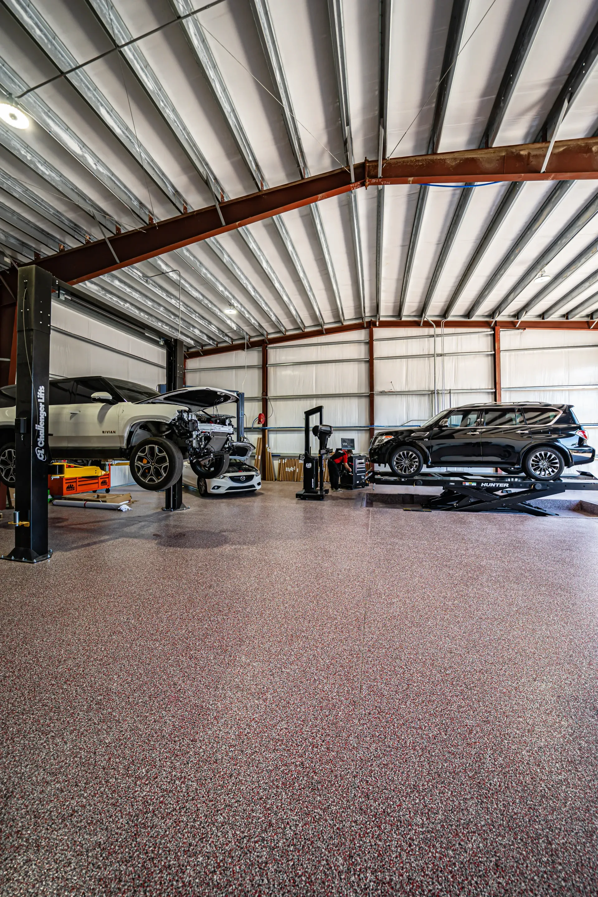 Vehicles on lifts in a mechanics shop with speckled floor, metal beams, and open space. | Advance Automotive