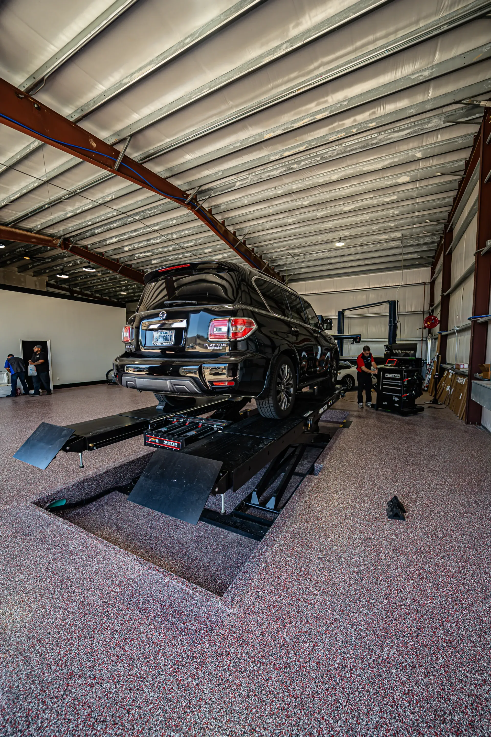 Black SUV on a lift in a garage with people working. | Advance Automotive
