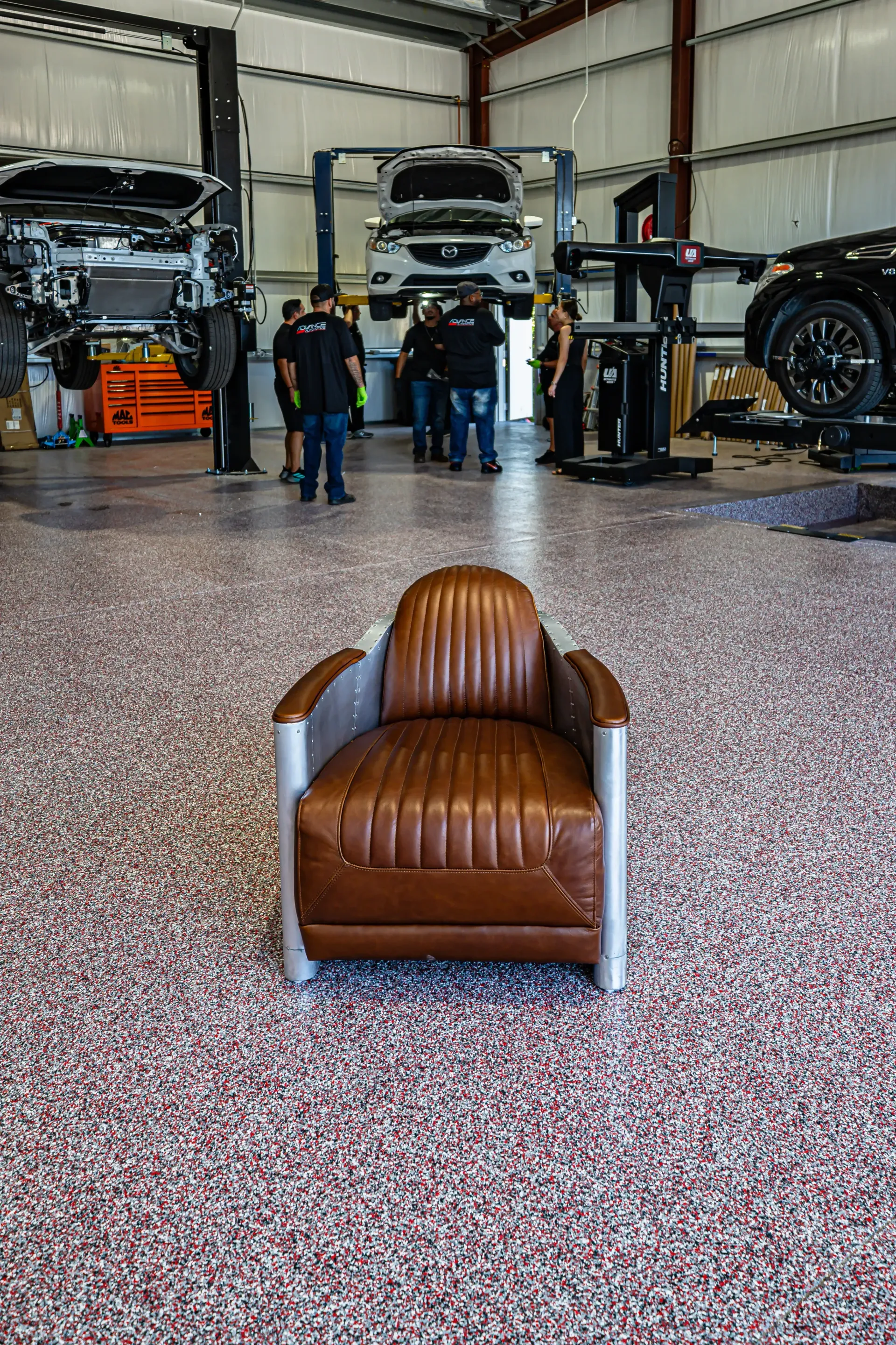 Brown leather armchair in a mechanic shop with people and cars on lifts. | Advance Automotive