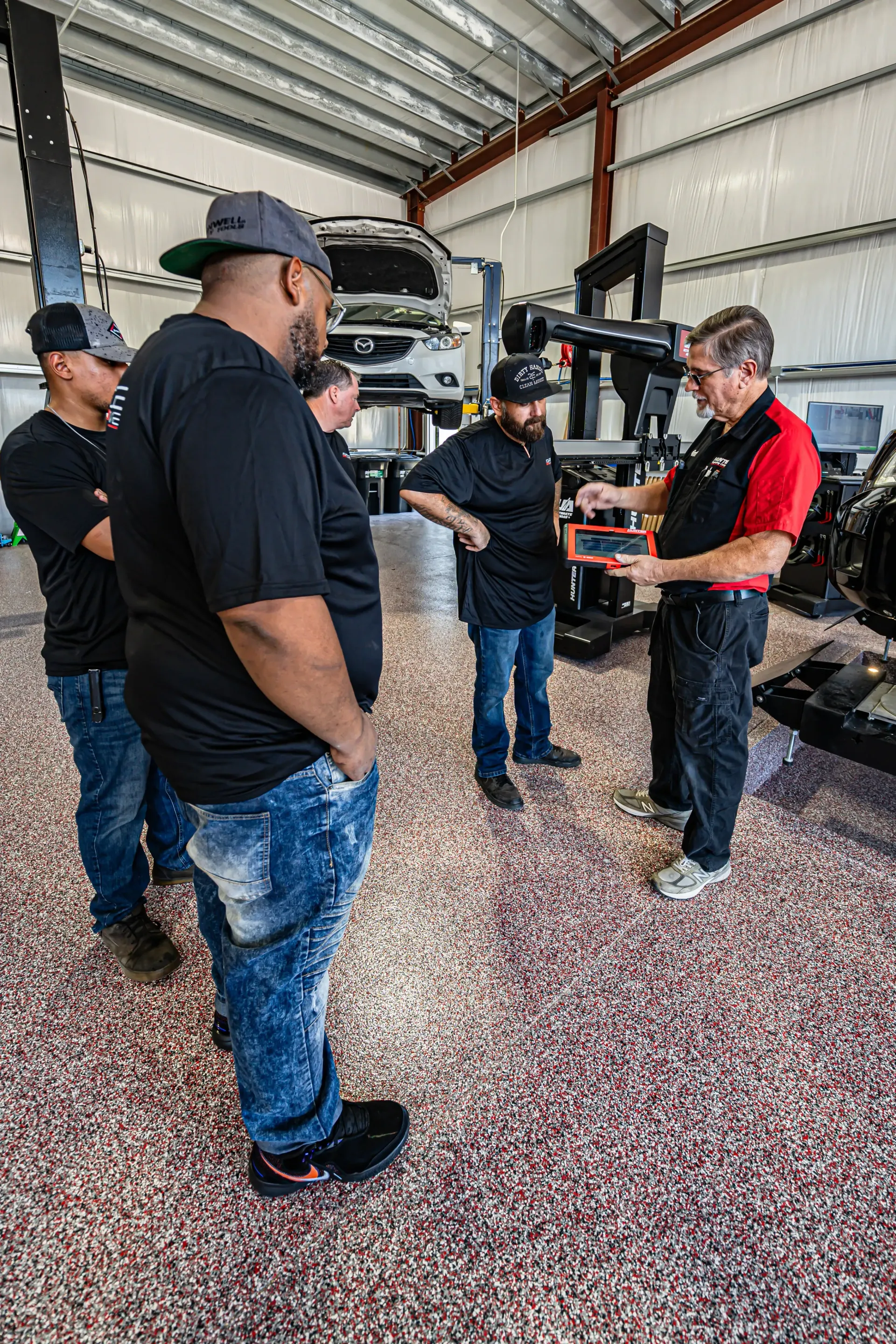 Group of men in a garage looking at a device, possibly car repair training. | Advance Automotive