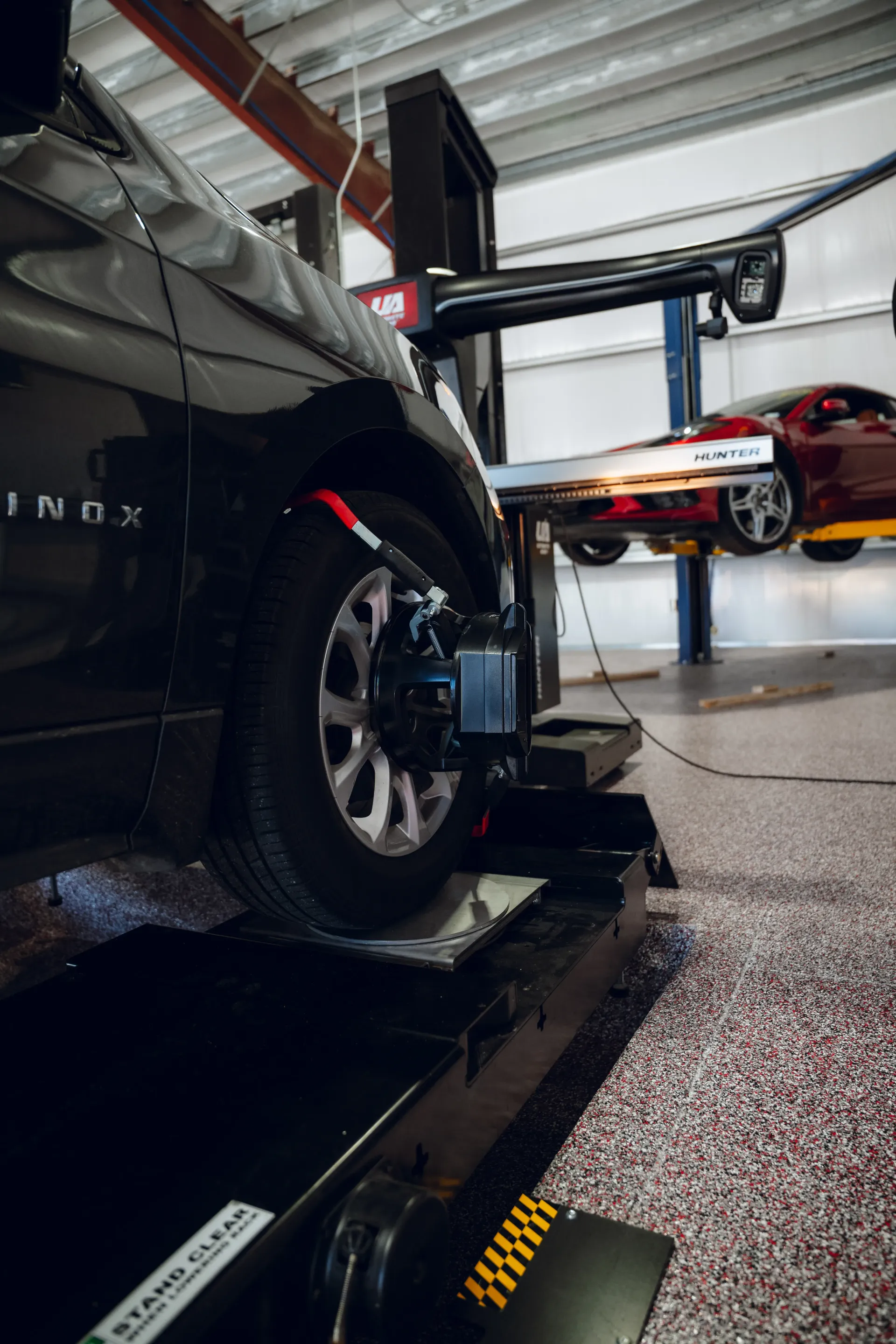 Car tire being aligned on a lift in a garage. Another red car is visible in the background. | Advance Automotive