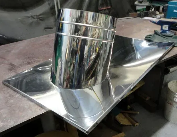 Section de conduit métallique brillant sur une surface en tôle réfléchissante dans un atelier.