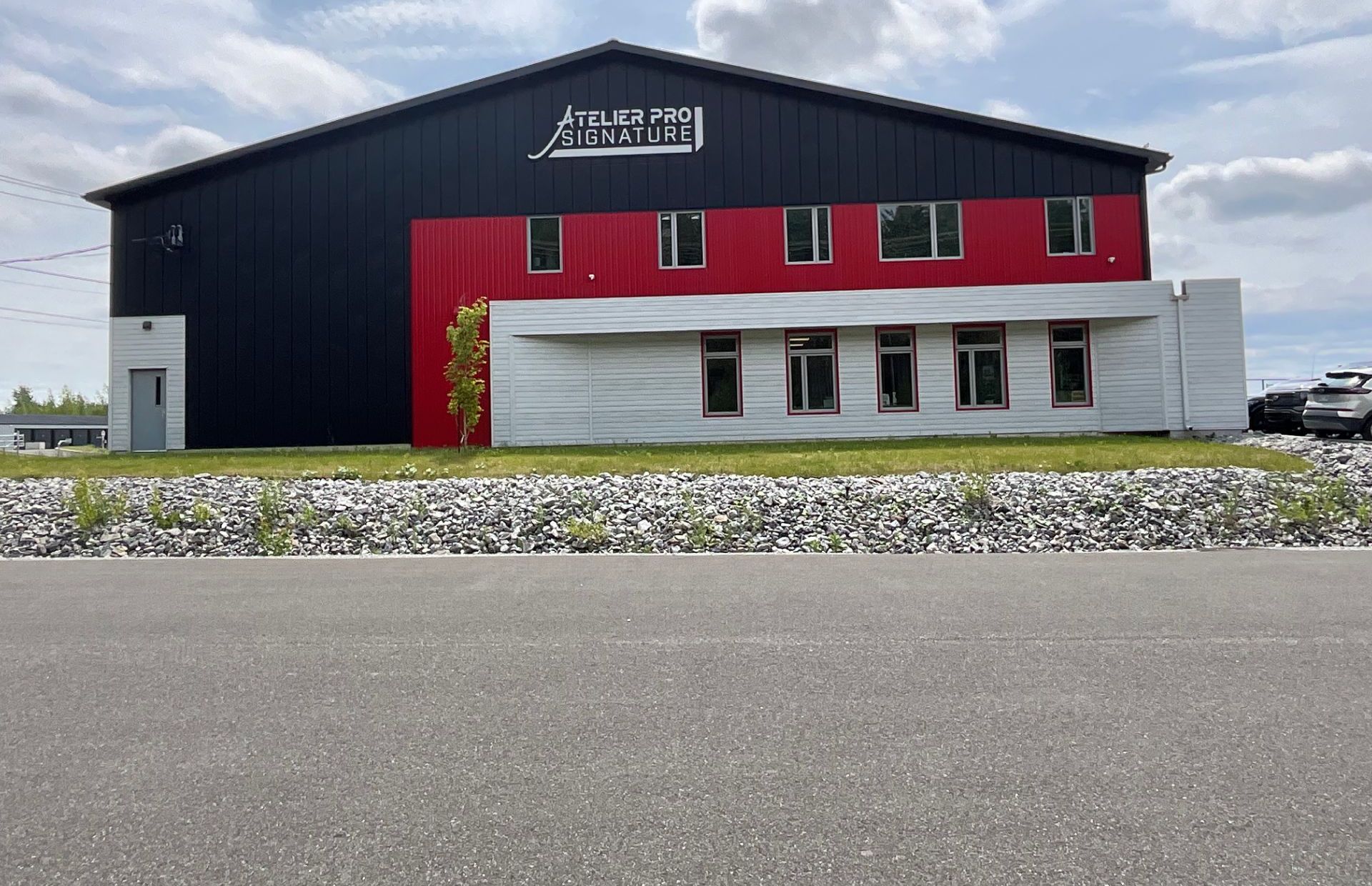 Bâtiment moderne noir, rouge et blanc vu de l'autre côté d'un parking vide sous un ciel nuageux.