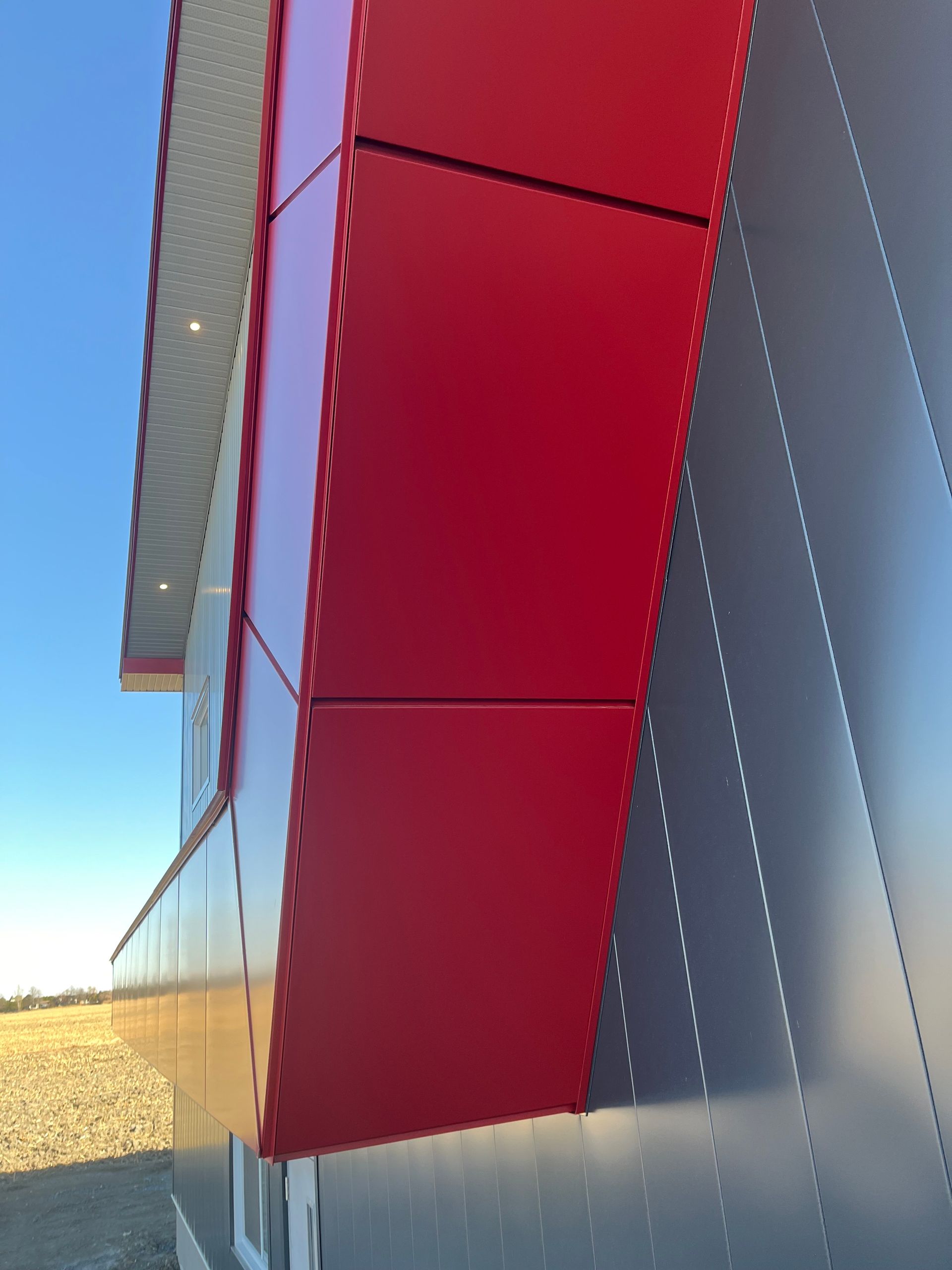 Façade d'un bâtiment moderne avec panneaux rouges et bardage métallique gris au soleil