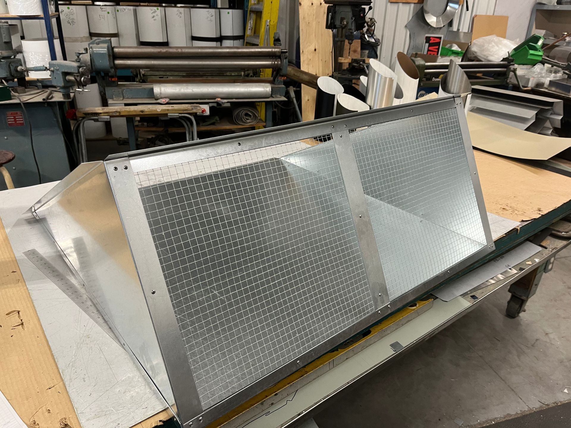 Panneaux métalliques perforés sur un établi dans un atelier, avec des outils et des machines en arrière-plan.