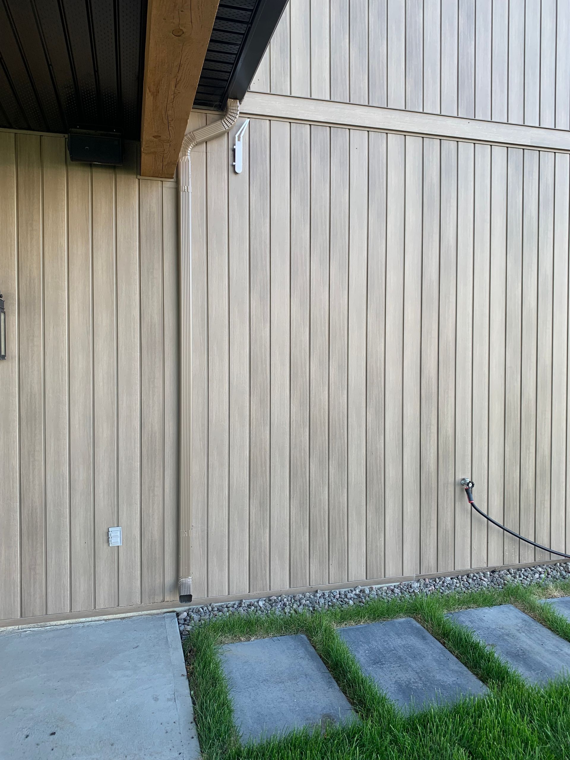 Mur extérieur en bois et patio couvert avec allée en béton et petites dalles de gazon