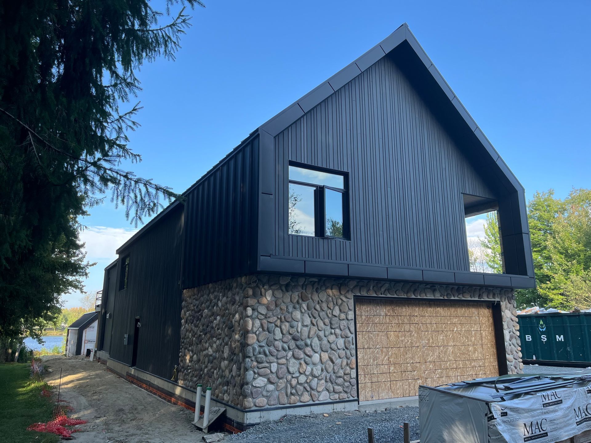 Extérieur d'une maison moderne à deux étages avec bardage foncé, murs inférieurs en pierre et entrée de garage condamnée.