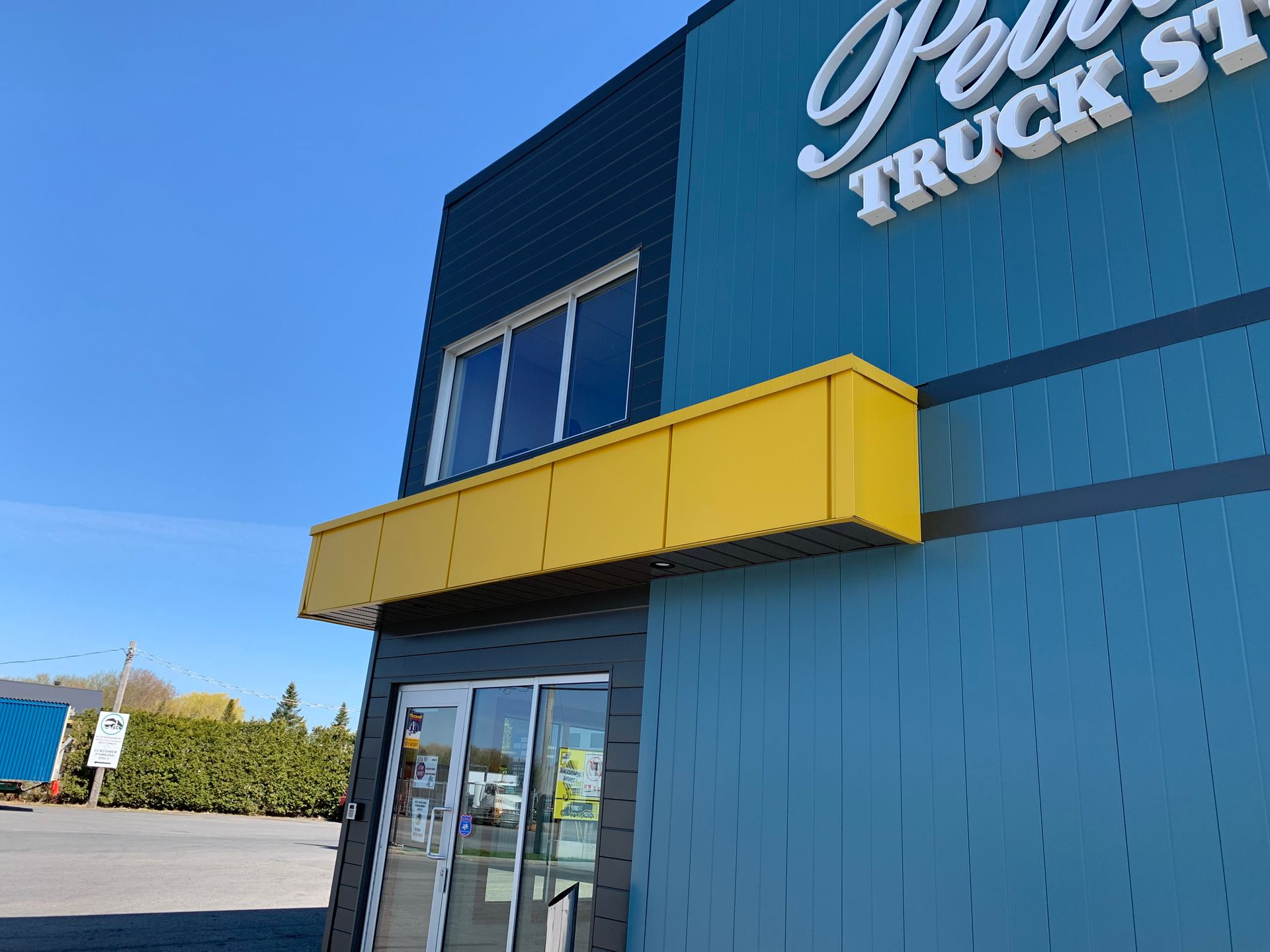 Bâtiment bleu d'aire de repos pour camions avec auvent jaune et entrée vitrée sous un ciel dégagé