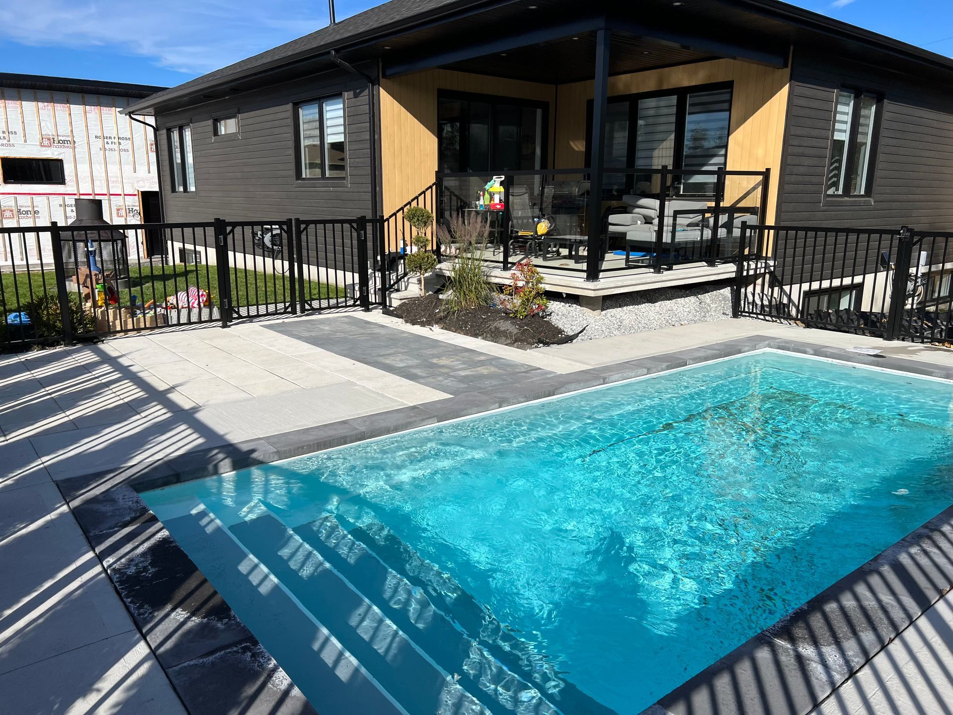 Patio de maison moderne avec une petite piscine turquoise, des balustrades noires et un coin salon près d'une terrasse en bois.