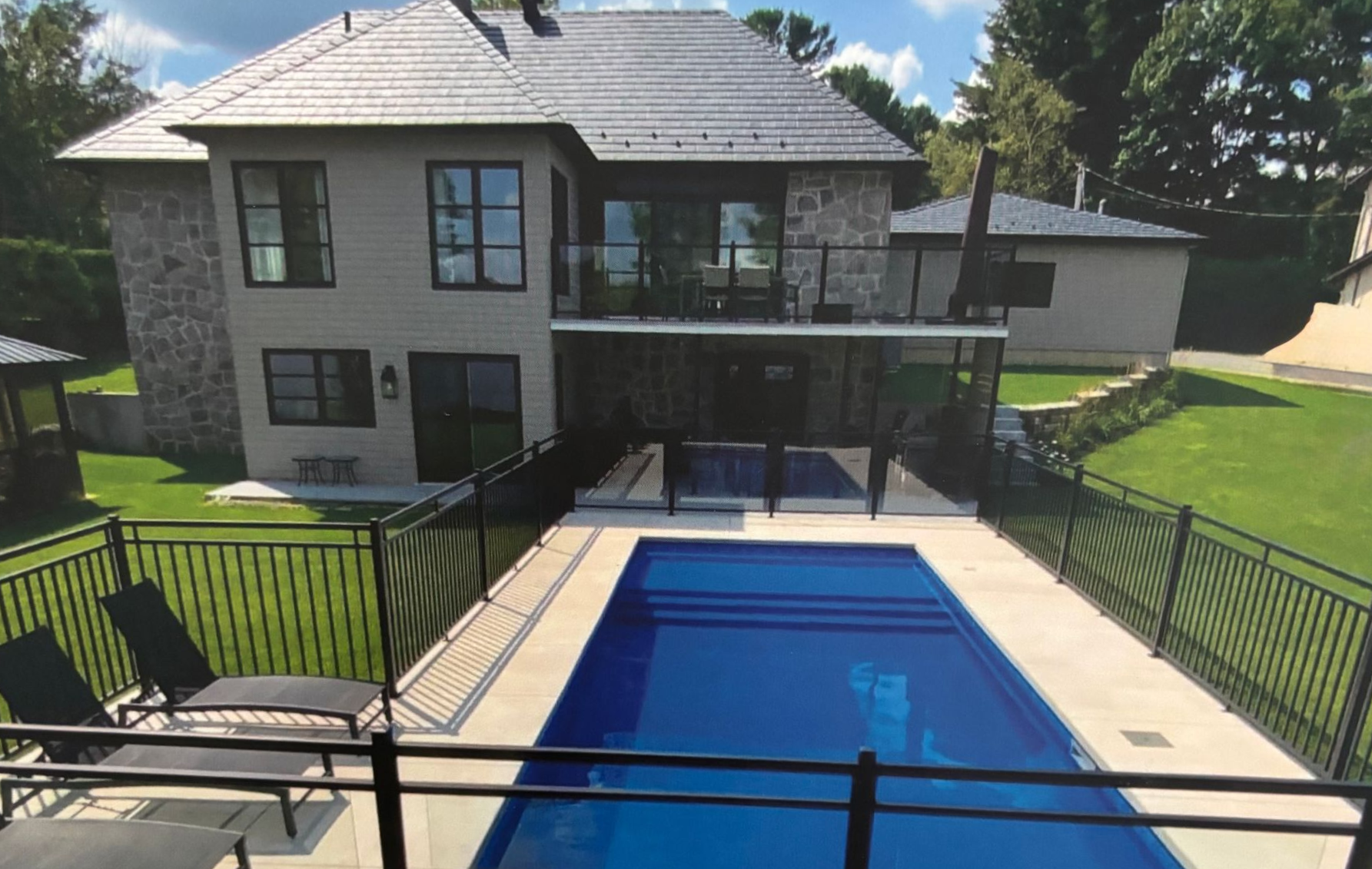 Maison moderne avec une piscine rectangulaire bleue dans le jardin, visible depuis la terrasse.