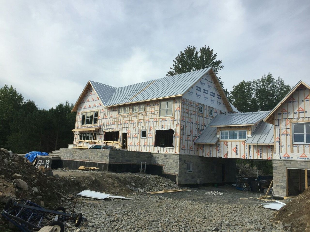 Maison partiellement construite avec toit en métal et charpente apparente sur un chantier boueux