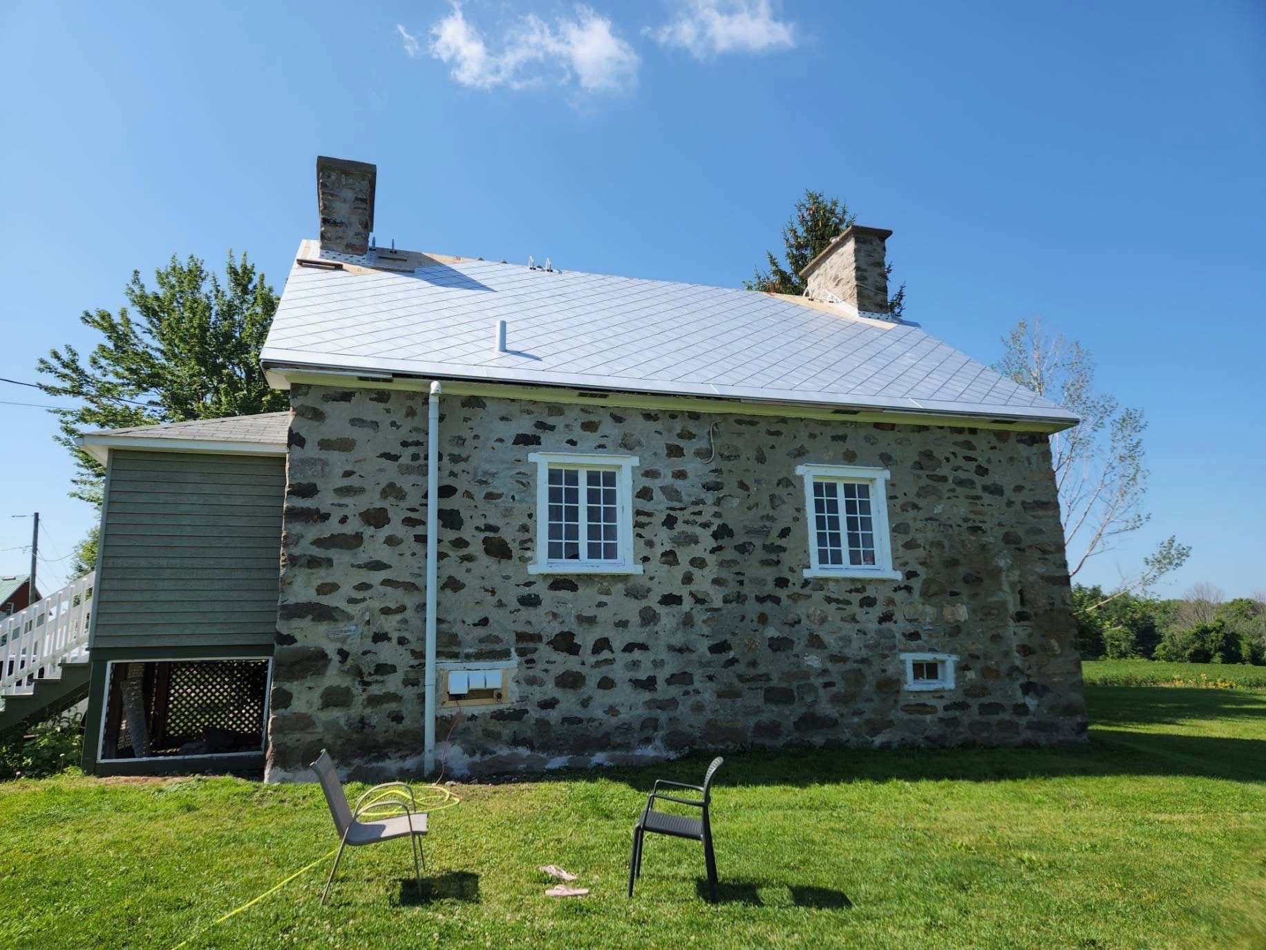 Maisonnette en pierre au toit blanc et aux volets bleus, sur une pelouse verdoyante sous un ciel dégagé.