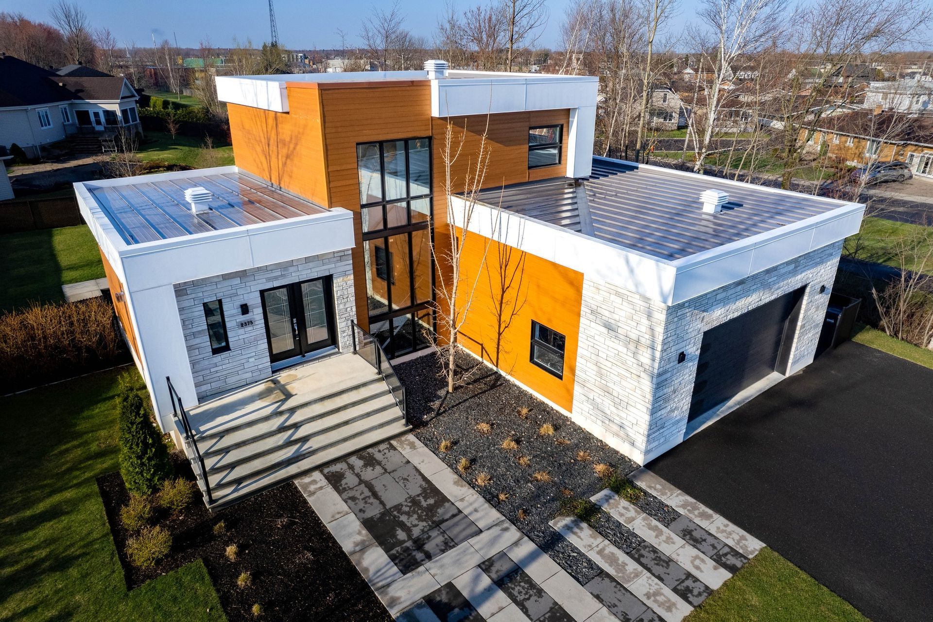 Maison moderne blanche et orange avec de grandes fenêtres et une allée pavée à l'avant par une journée ensoleillée