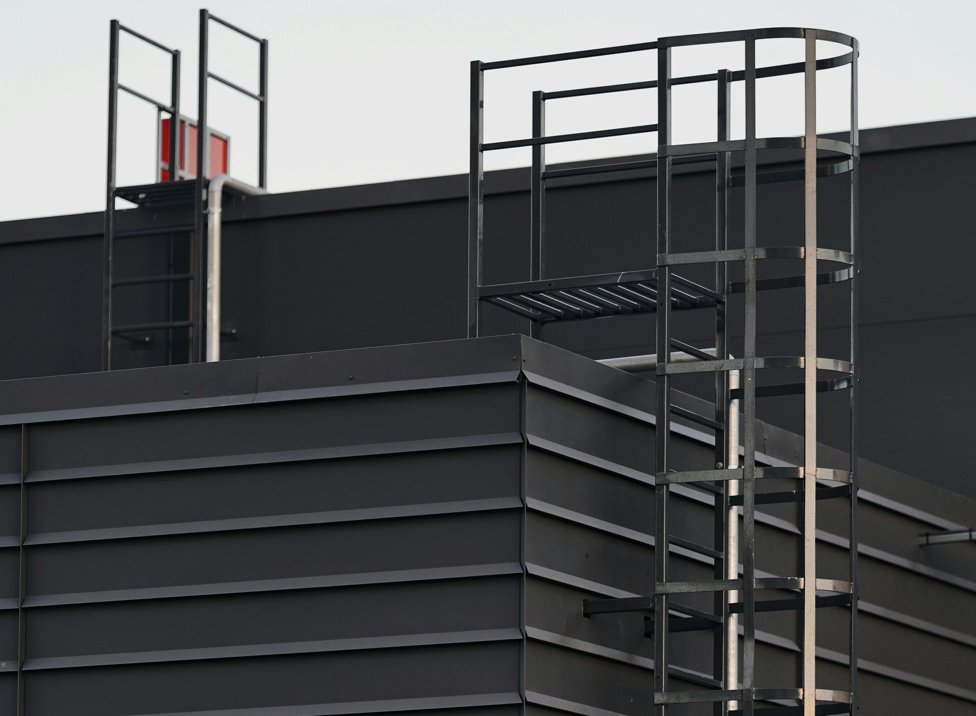 Rooftop industrial ladder against a dark Tanque Verde metal building with black railings and platforms
