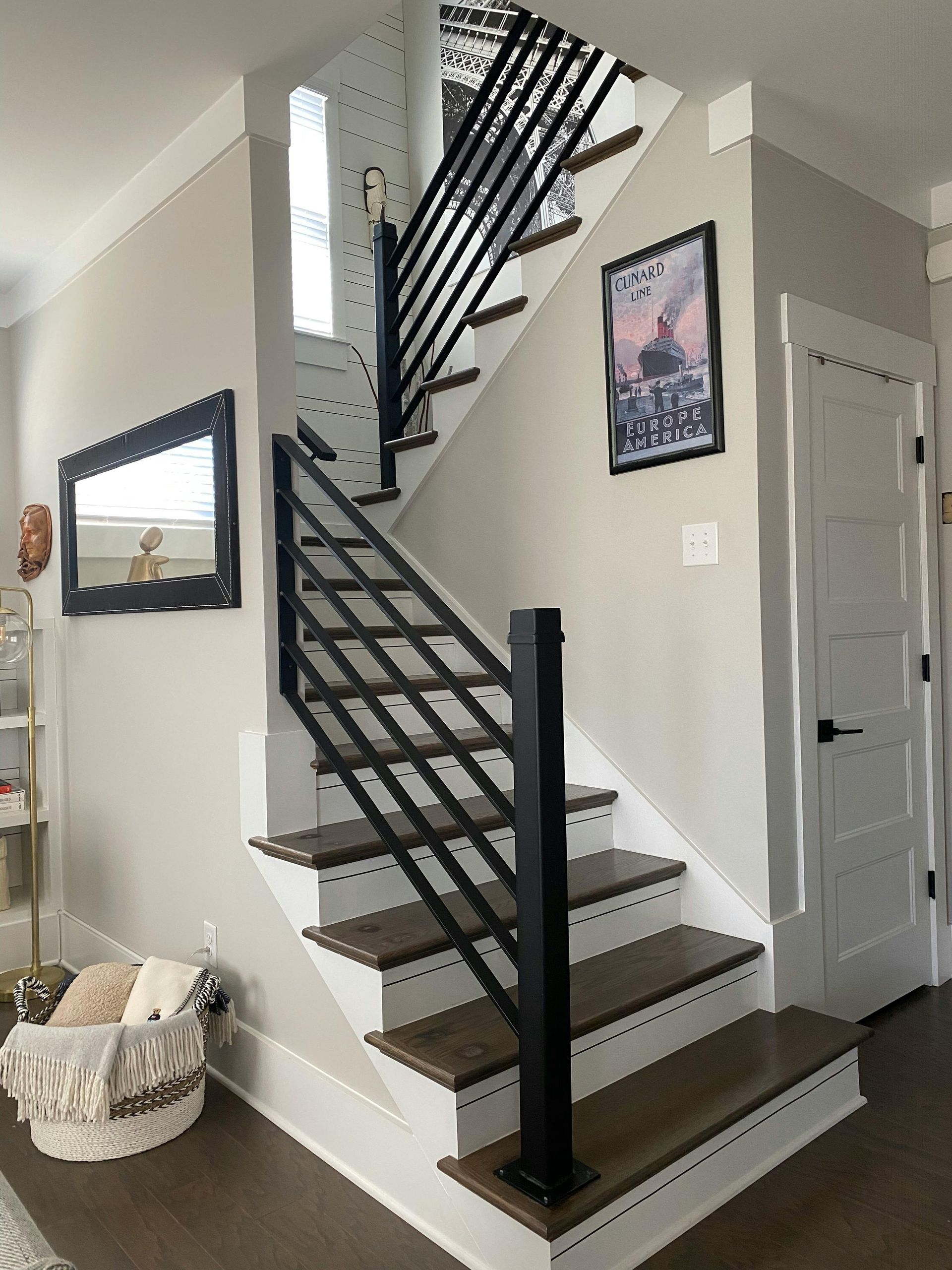 Staircase with black railings in a gray home interior, beside a white door and wall art.