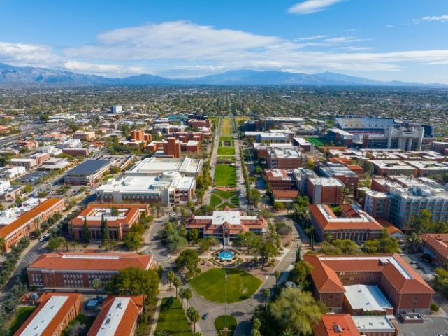 Aerial view of the University of Arizona campus with red-brick buildings and mountains in the distance.