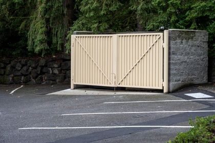 Beige metal gate, vertical bars, mounted on concrete with stone walls