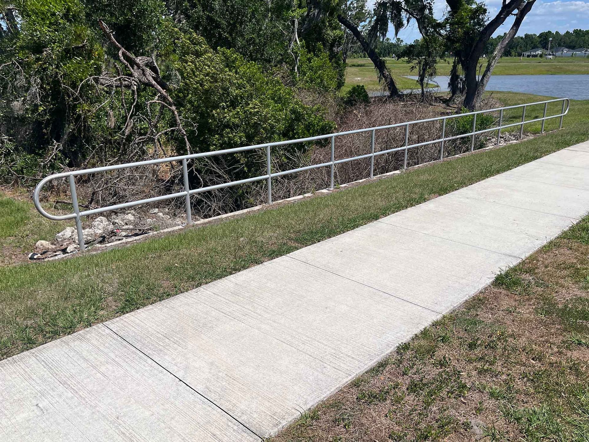 Sidewalk beside a grassy ditch with a white metal railing and trees along a Marana roadside