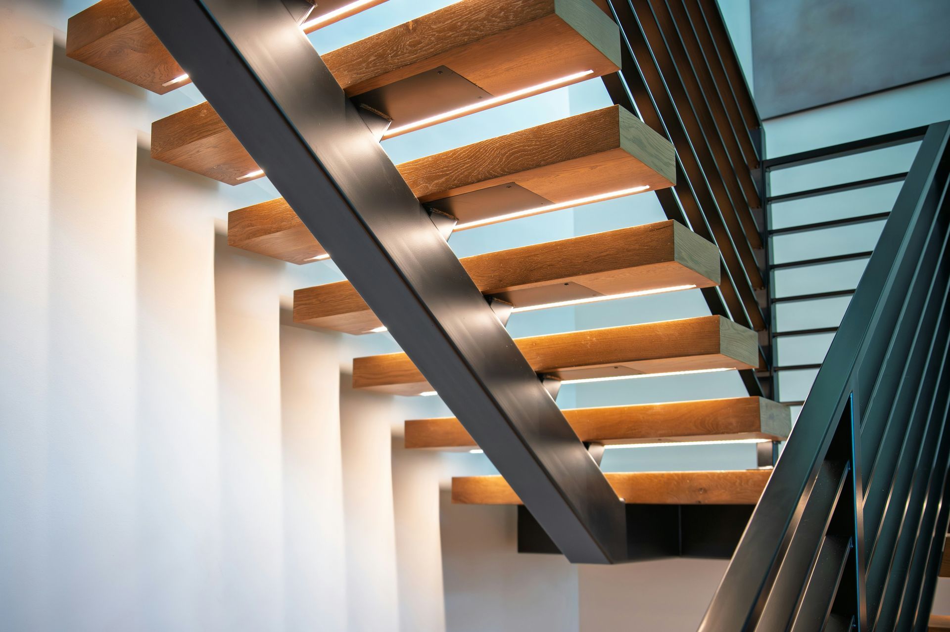 Modern staircase with wooden steps, dark metal railings, and white walls in a bright interior