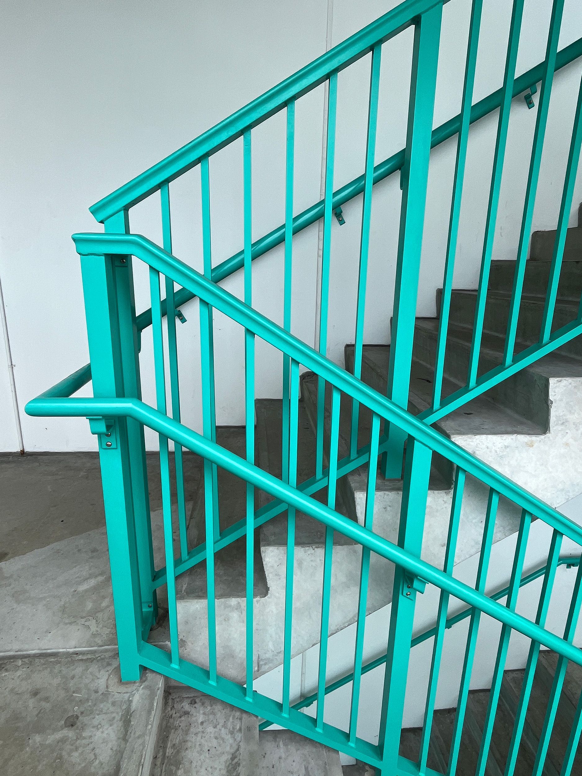 Teal metal handrails and balusters on gray concrete stairs
