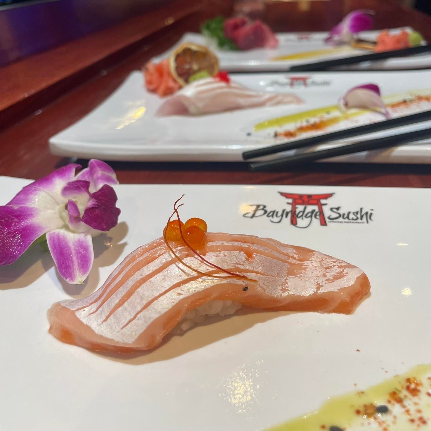 Sushi platter with salmon nigiri and orchid garnish on a white plate at a restaurant table