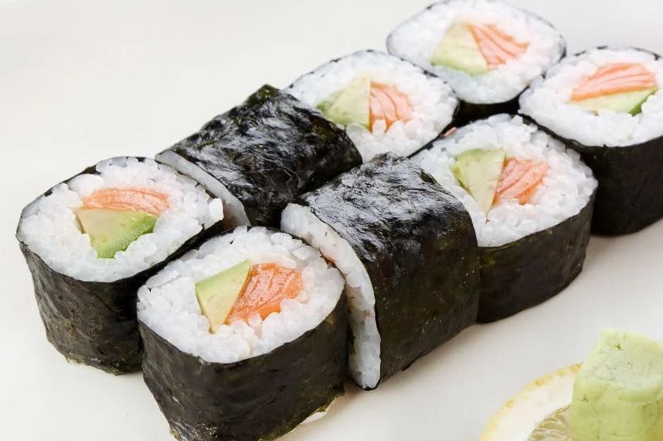 Sushi rolls with salmon, avocado, and rice on a white plate, one roll wrapped in seaweed
