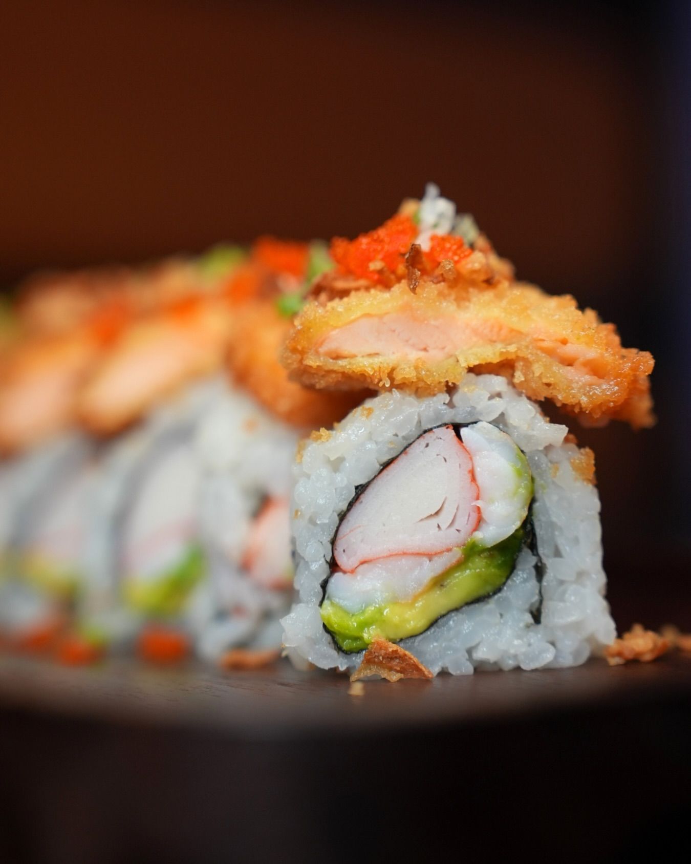 Close-up of sushi rolls topped with salmon and orange roe on a dark plate