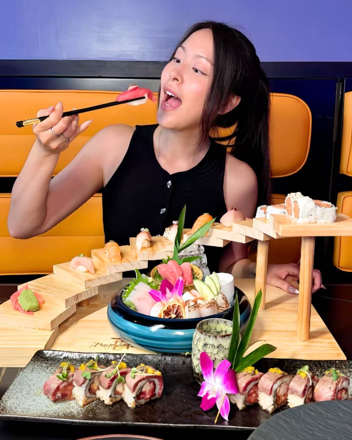 Woman eating sushi at a restaurant table with a wooden boat platter and colorful garnishes