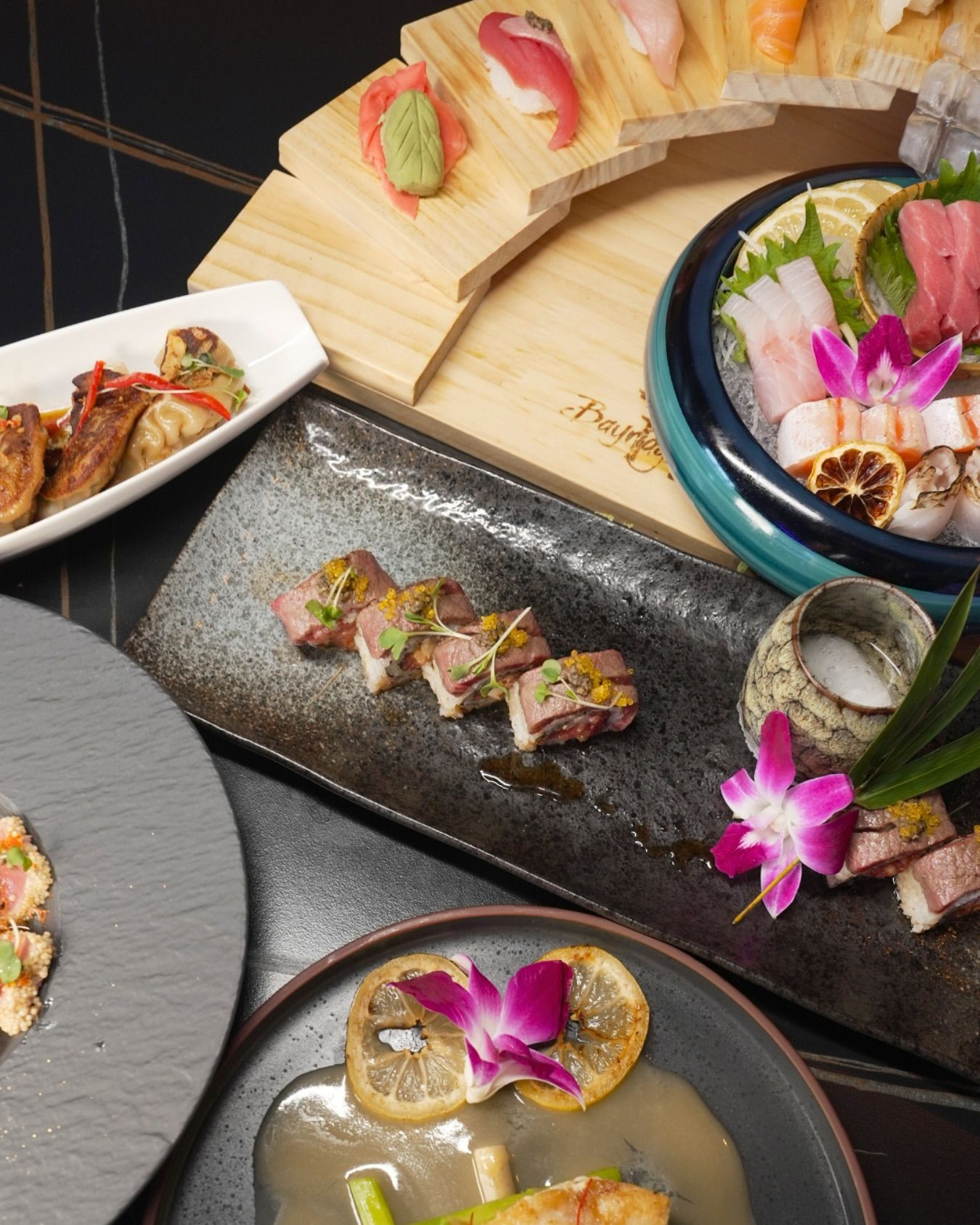 Assorted Japanese sushi and sashimi platters with flowers on a dark table