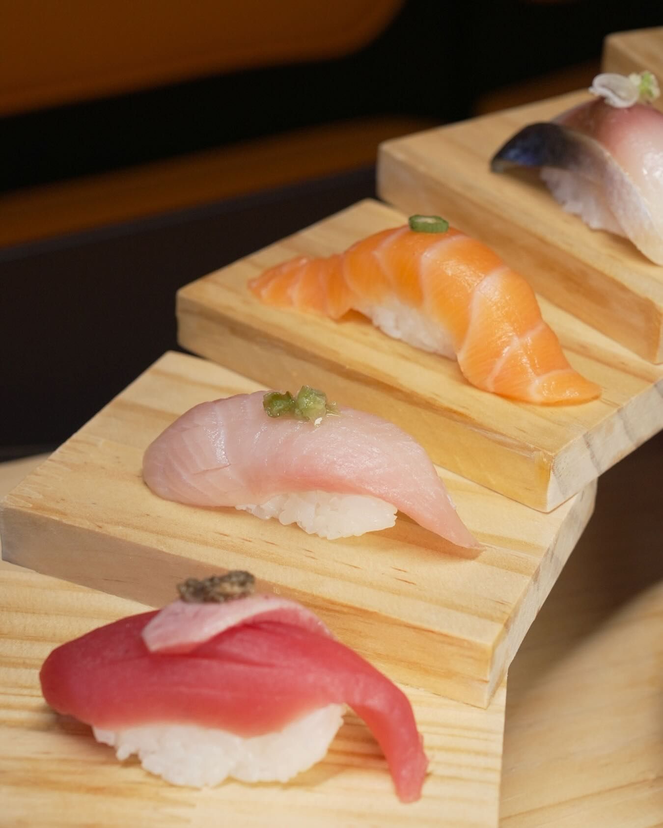 Assorted sushi nigiri on wooden steps, including red tuna, pale fish, and orange salmon pieces.
