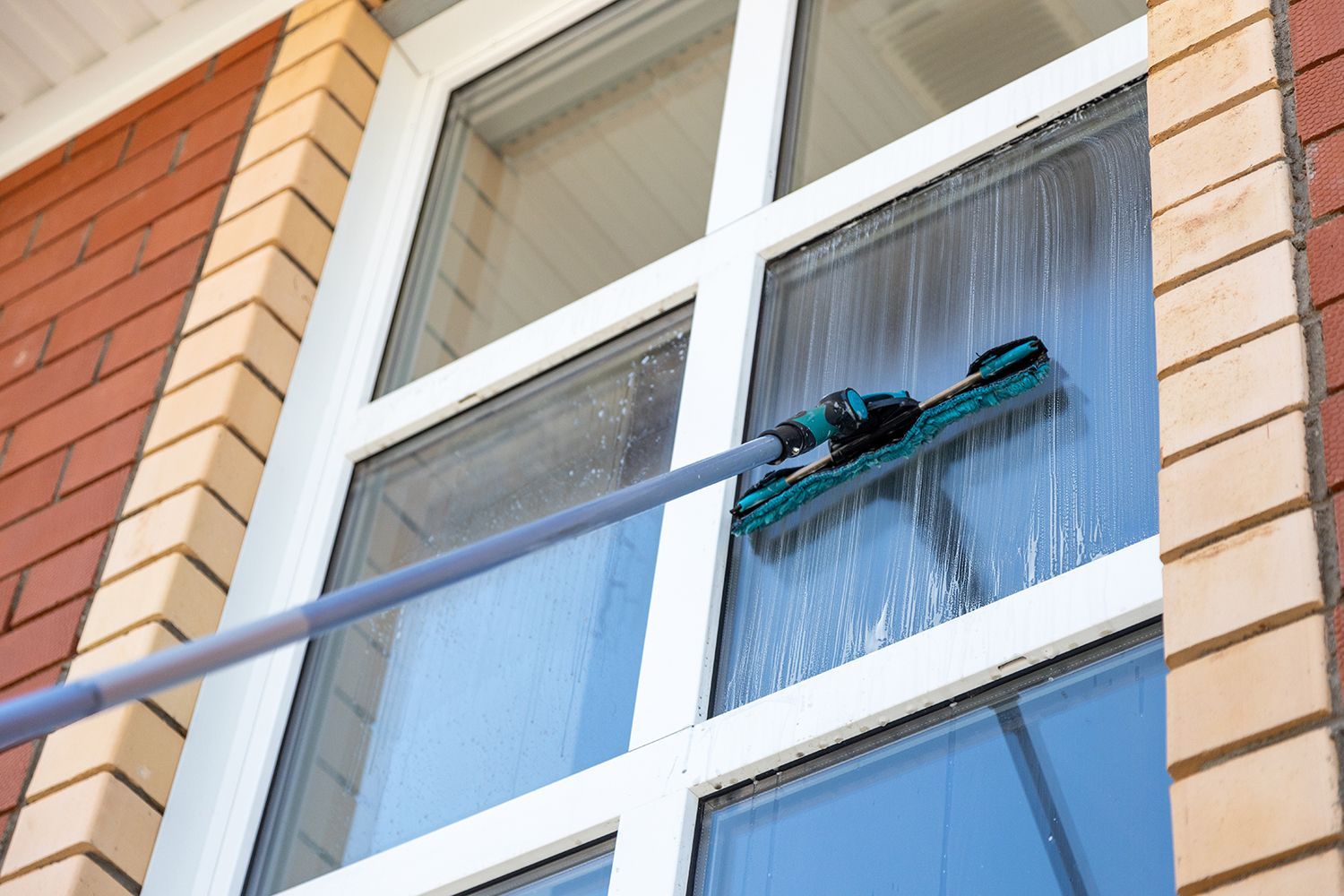 Person washing an upper-story window with a long-handled squeegee