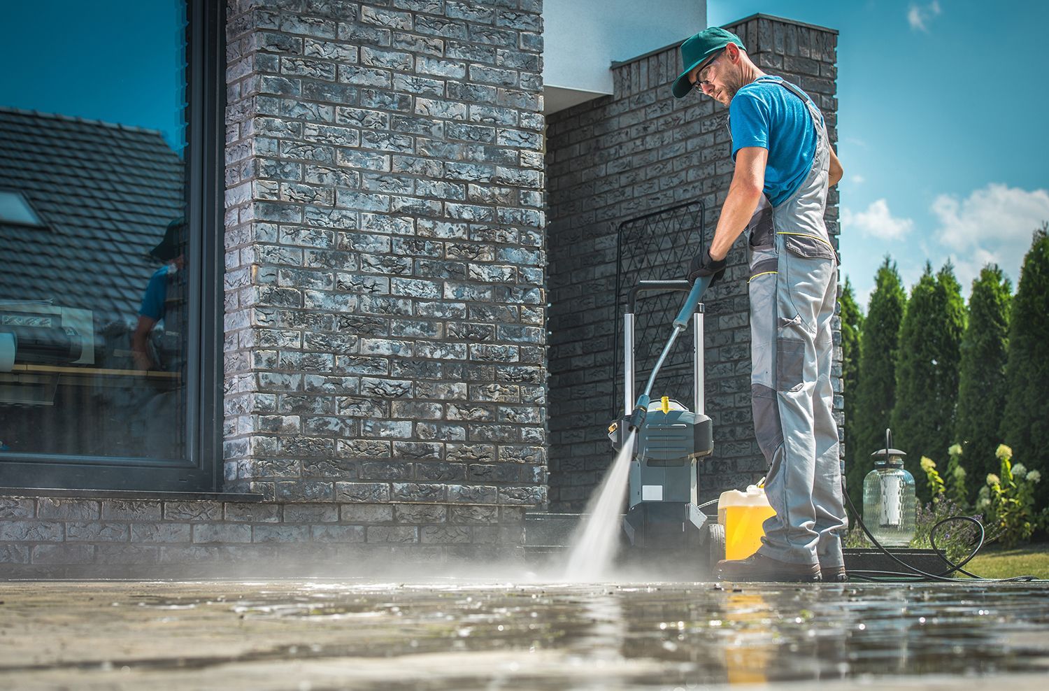 Person pressure-washing a brick house patio with a blue and yellow cleaner