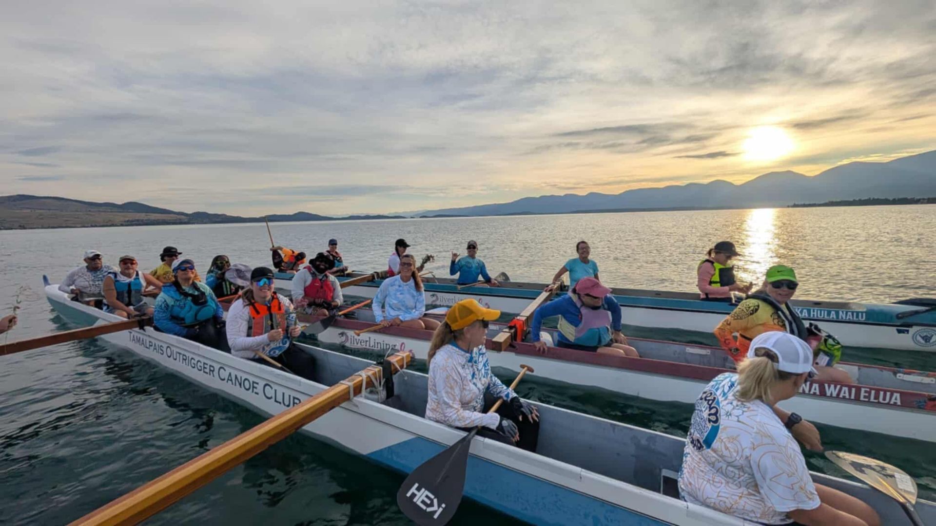 People in canoes paddling on a lake at sunset.