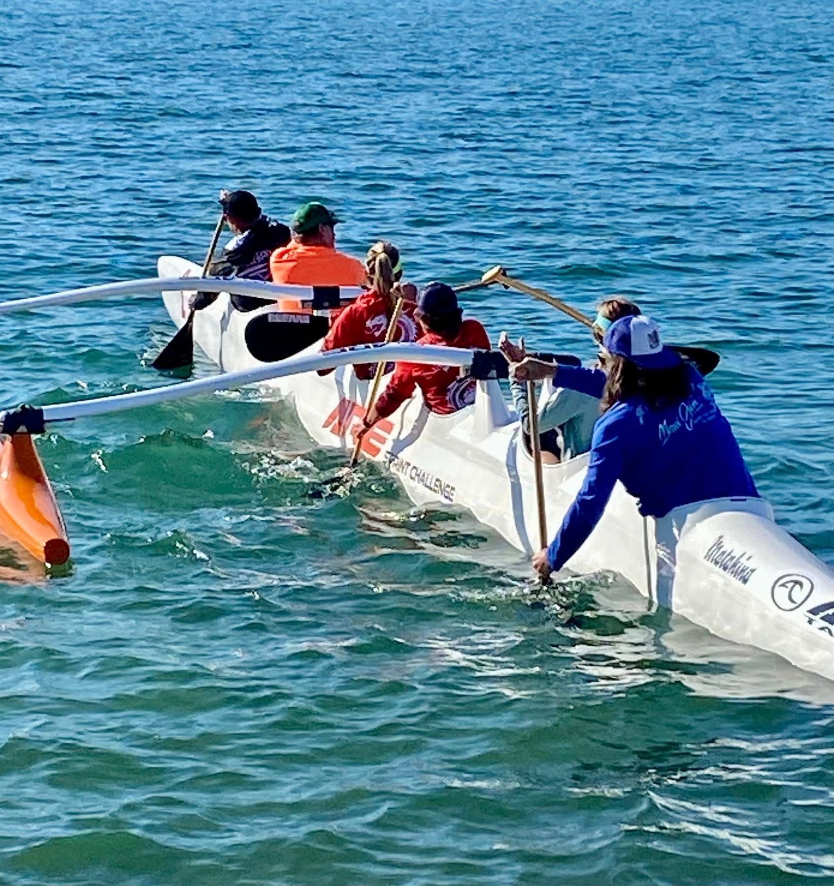 Outrigger canoe with a team of paddlers in blue water on a sunny day.