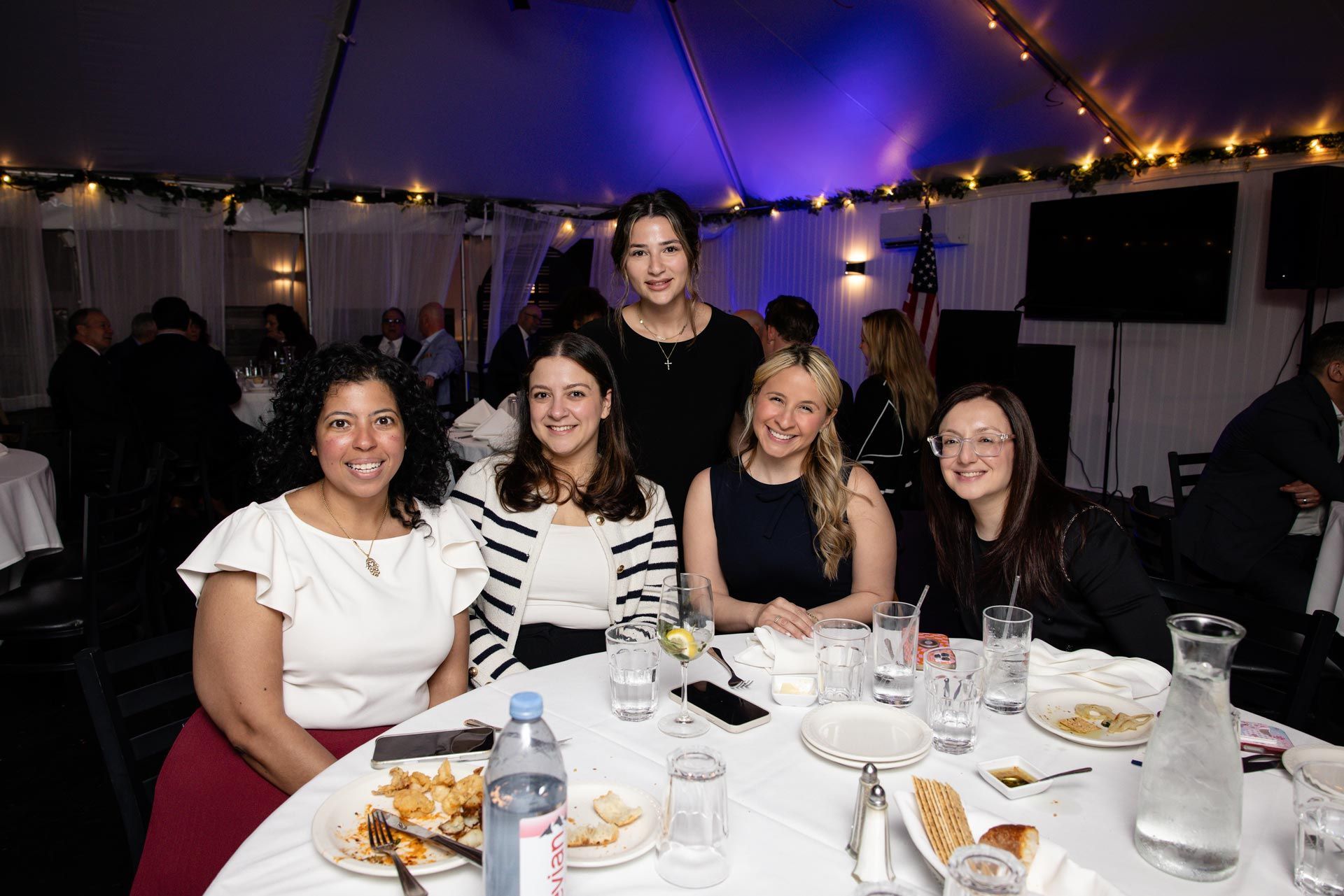 Five people smiling at a decorated banquet table under purple lights at an indoor event