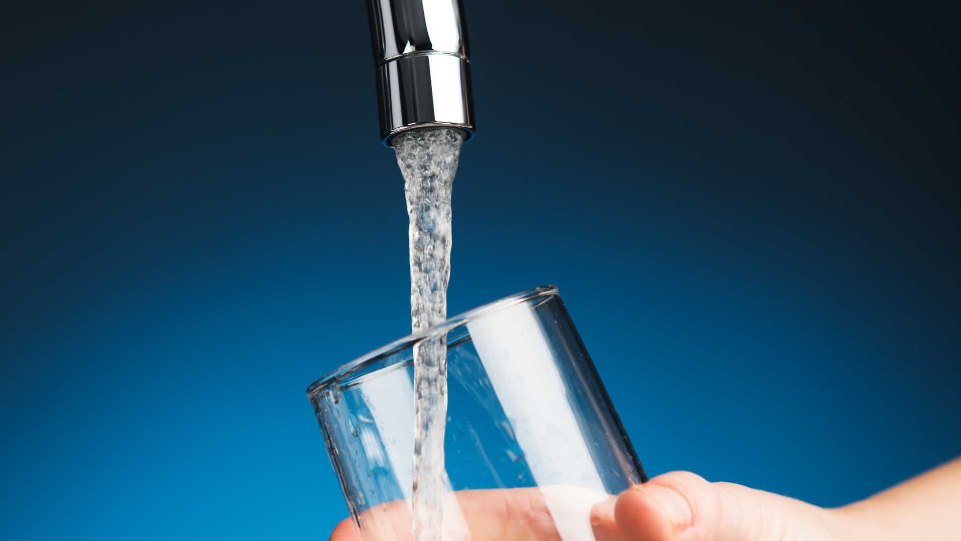 A person is pouring water into a glass from a faucet.