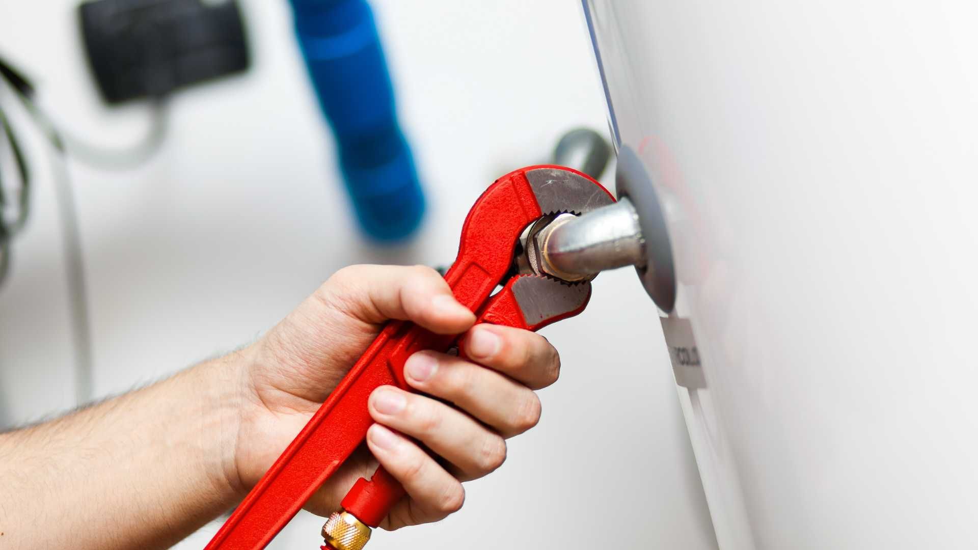 A person is fixing a water heater with a wrench.