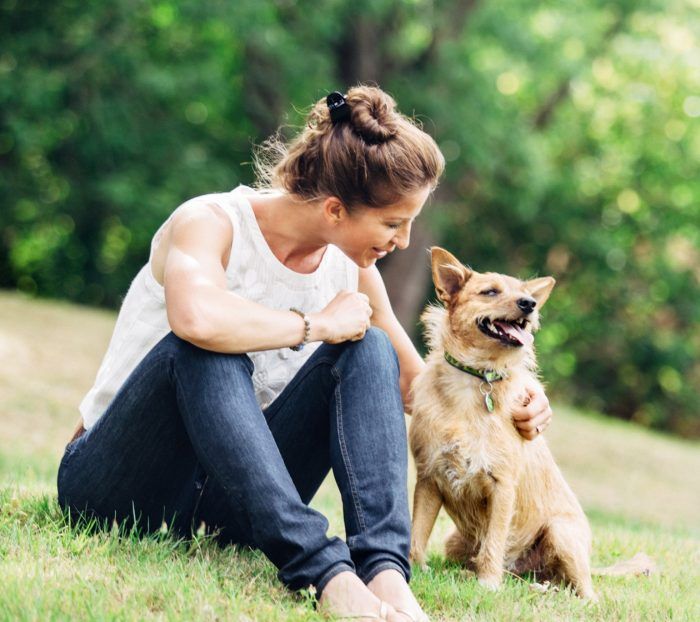 A woman is sitting on the grass with her dog.