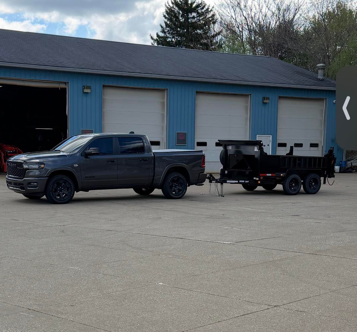 Dark pickup truck towing a small trailer in front of a blue garage with white doors