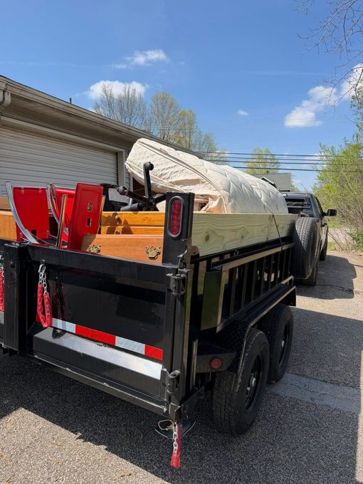 Black utility trailer loaded with debris bags and red equipment, parked on a gravel driveway under a blue sky