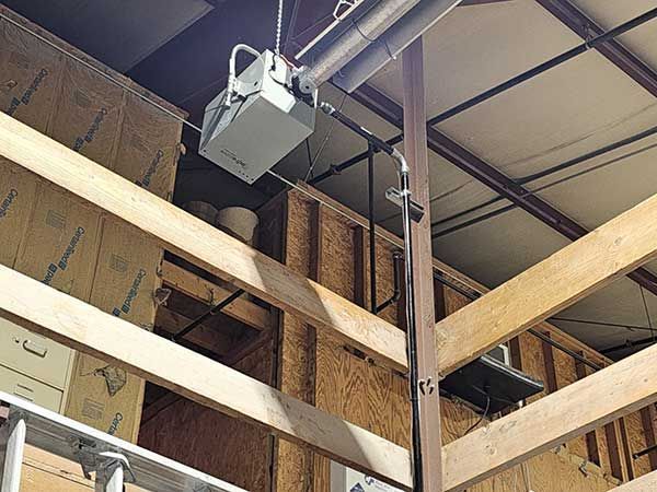 Warehouse ceiling with suspended garage door opener, beams, and stacked cardboard boxes
