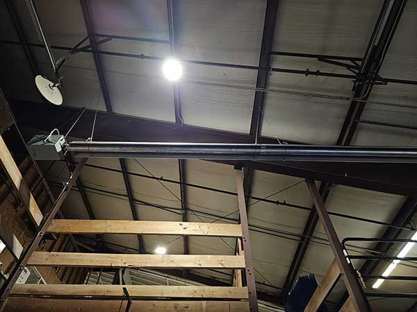 Indoor industrial ceiling with exposed beams, bright lights, and a wooden staircase railing below